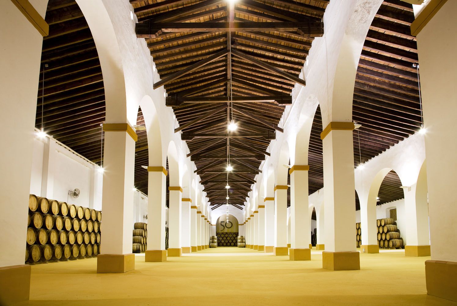 Nave de crianza con arcos encalados, vigas de madera y botas de roble